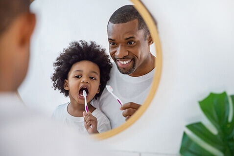 Father teaching child to brush teeth